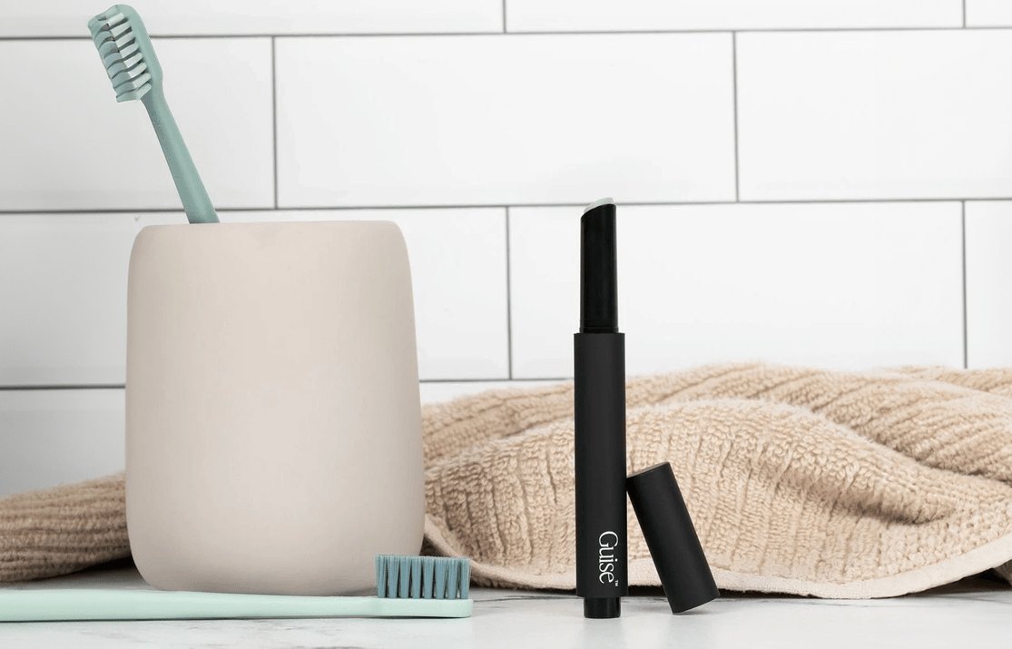 A Guise stick on a bathroom counter next to a toothbrush cup